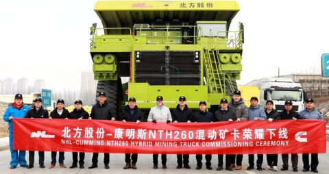 Eine Gruppe von Cummins-Mitarbeitern hält ein rotes Banner vor einem Hybrid-Lkw für den Bergbau