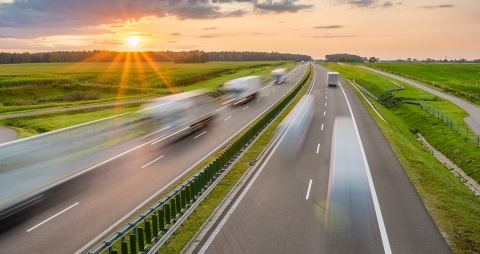 Vierspurige Autobahn bei Sonnenuntergang mit Sattelschleppern, die verschwommen darauf fahren