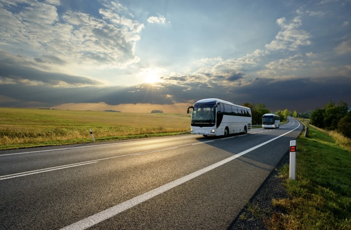 Bus driving down a flat road with the sun in the background