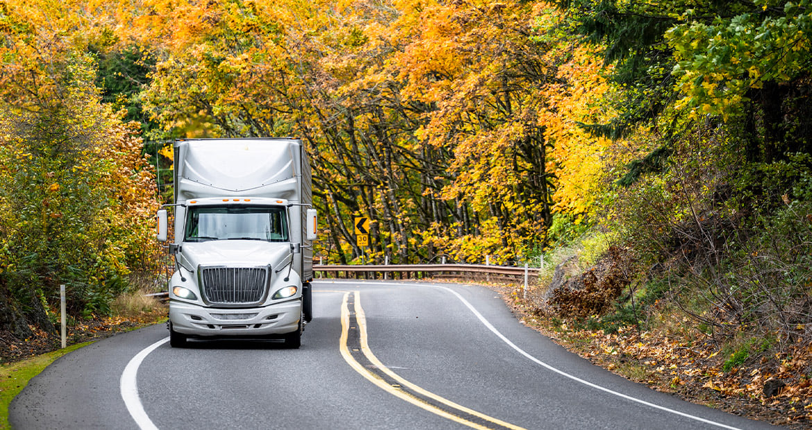Un semirremolque viaja por una carretera curva con follaje otoñal en el fondo y representa innovaciones avanzadas en motores de diésel