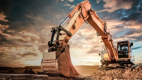 Se muestra una excavadora desenterrando tierra al atardecer