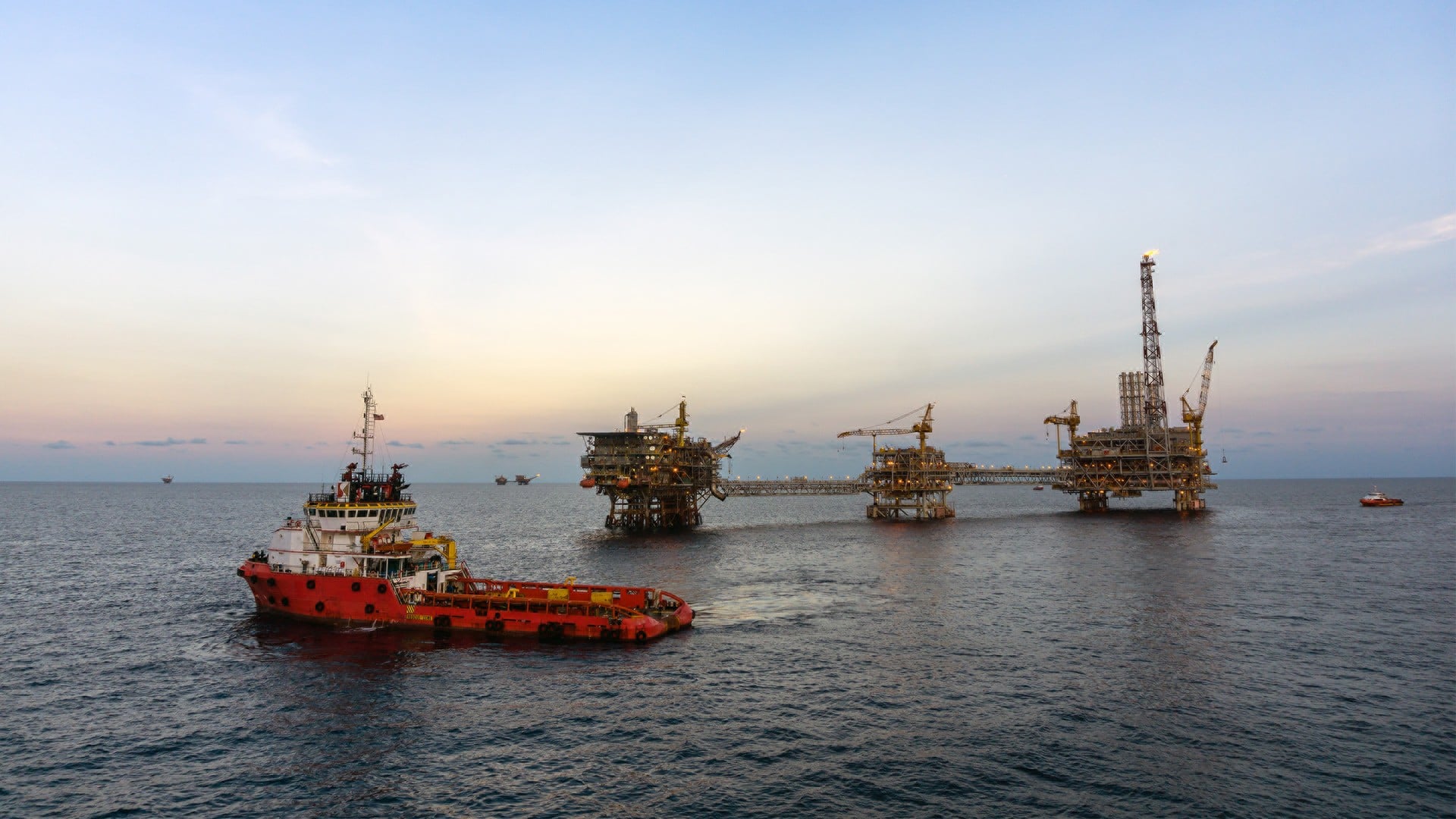 Un navire de ravitaillement s'approche d'une plateforme pétrolière en mer au coucher du soleil