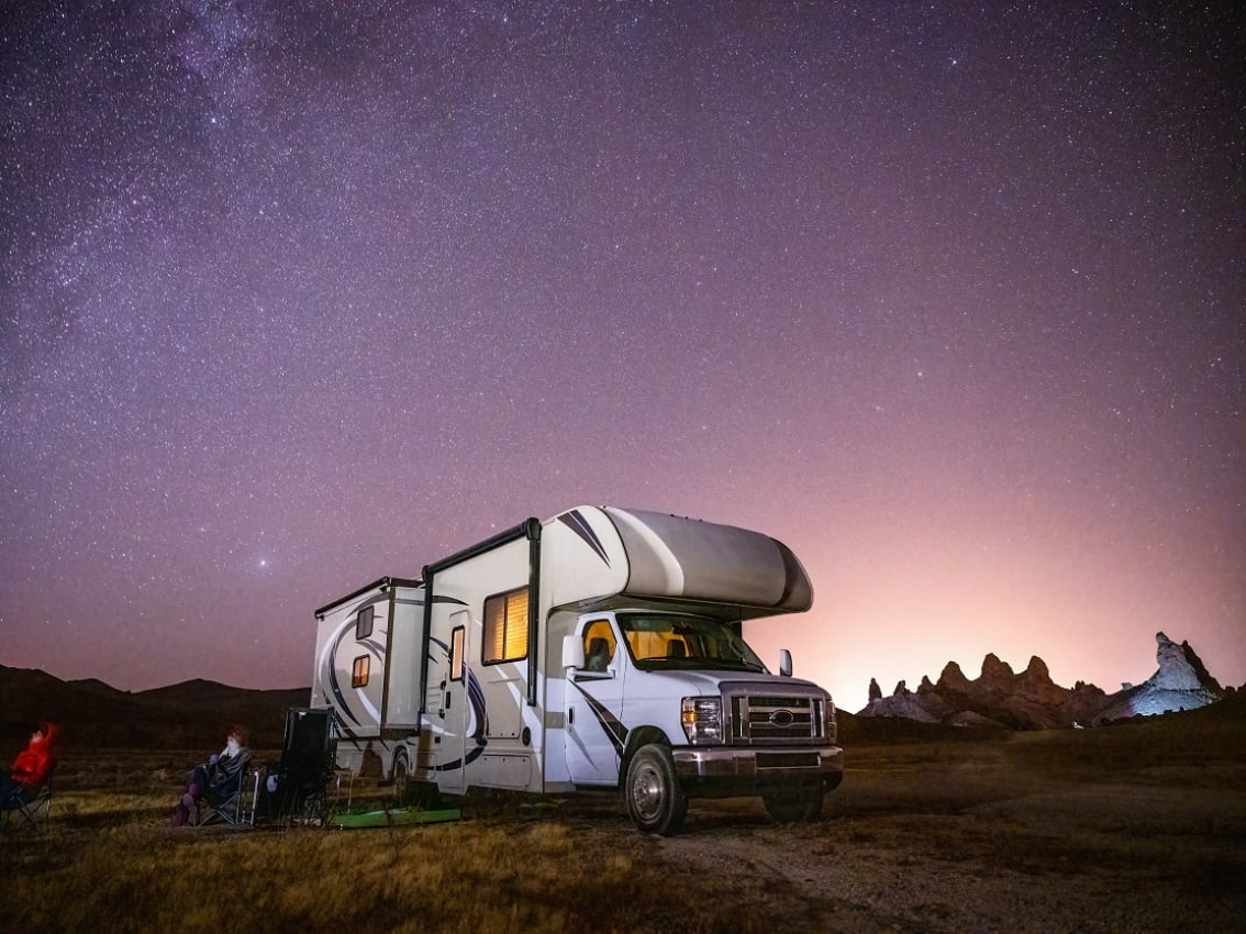 Camping-car dans un champ avec ciel nocturne en arrière-plan