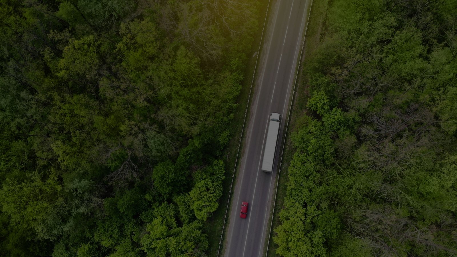 Vue aérienne d’un semi-remorque blanc et d’une voiture rouge circulant sur une autoroute à deux voies avec des arbres verts de chaque côté