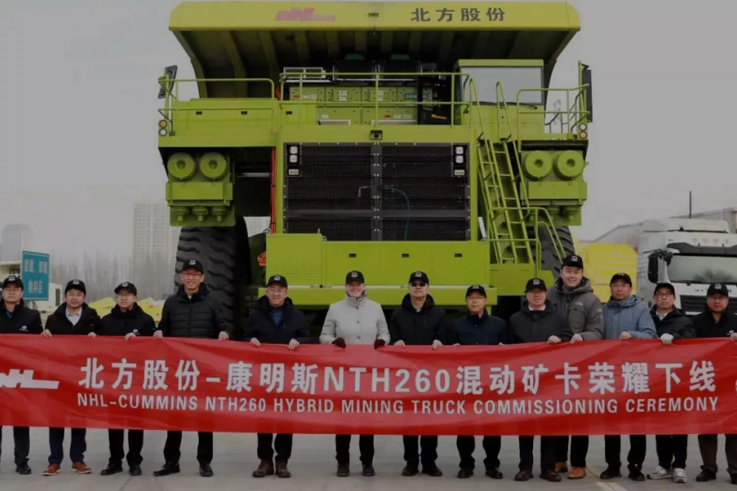 15 travailleurs de Cummins tenant une bannière rouge avec les mots NHL-Cummins NTH260 Hybrid Mining Truck Commissioning Cérémonie devant un grand véhicule d'exploitation minière