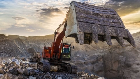 Grande excavatrice d'exploitation minière creusant des roches et du gravier au coucher du soleil