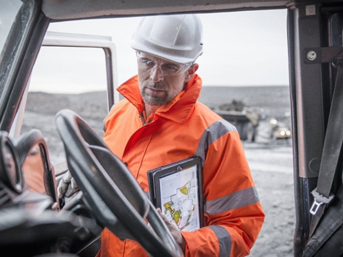 Un mineur muni d’un casque de sécurité et d’un équipement de protection examine une tablette dans un camion Un mineur muni d’un casque de sécurité et d’un équipement de protection examine une tablette dans un camion