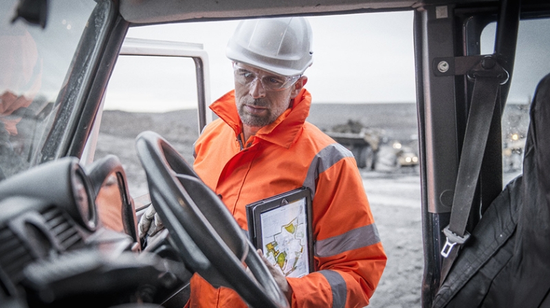 Un minero con casco y equipo de protección examina una tablet en un camión