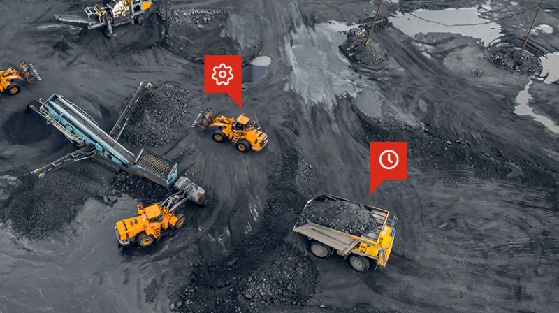 Vista aérea de vehículos de minería grandes en actividad, marcados con íconos de un engranaje y un reloj en color rojo