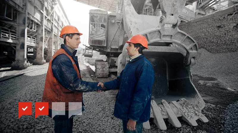 un profesional del área de minería dando la mano a otro frente a una excavadora