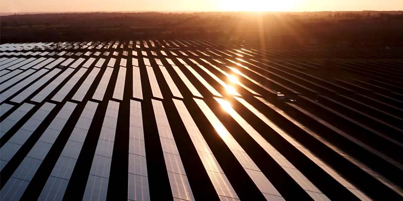 遠くに沈む太陽と太陽電池パネルが並ぶ発電施設