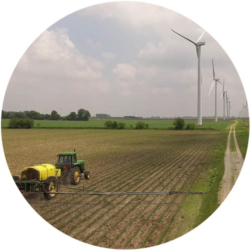 granja durante la cosecha, con un tractor y turbinas eólicas