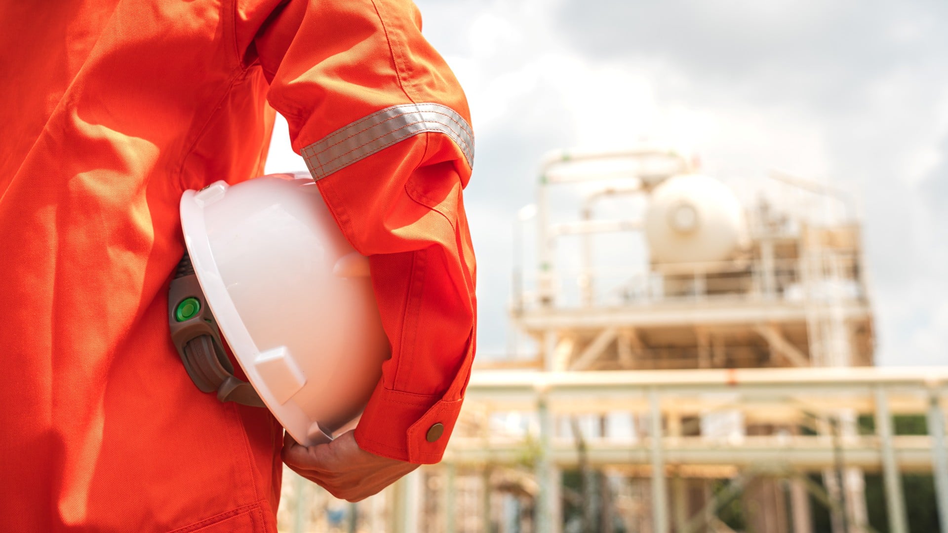 technician holding hard hat in arms while looking at oil rig