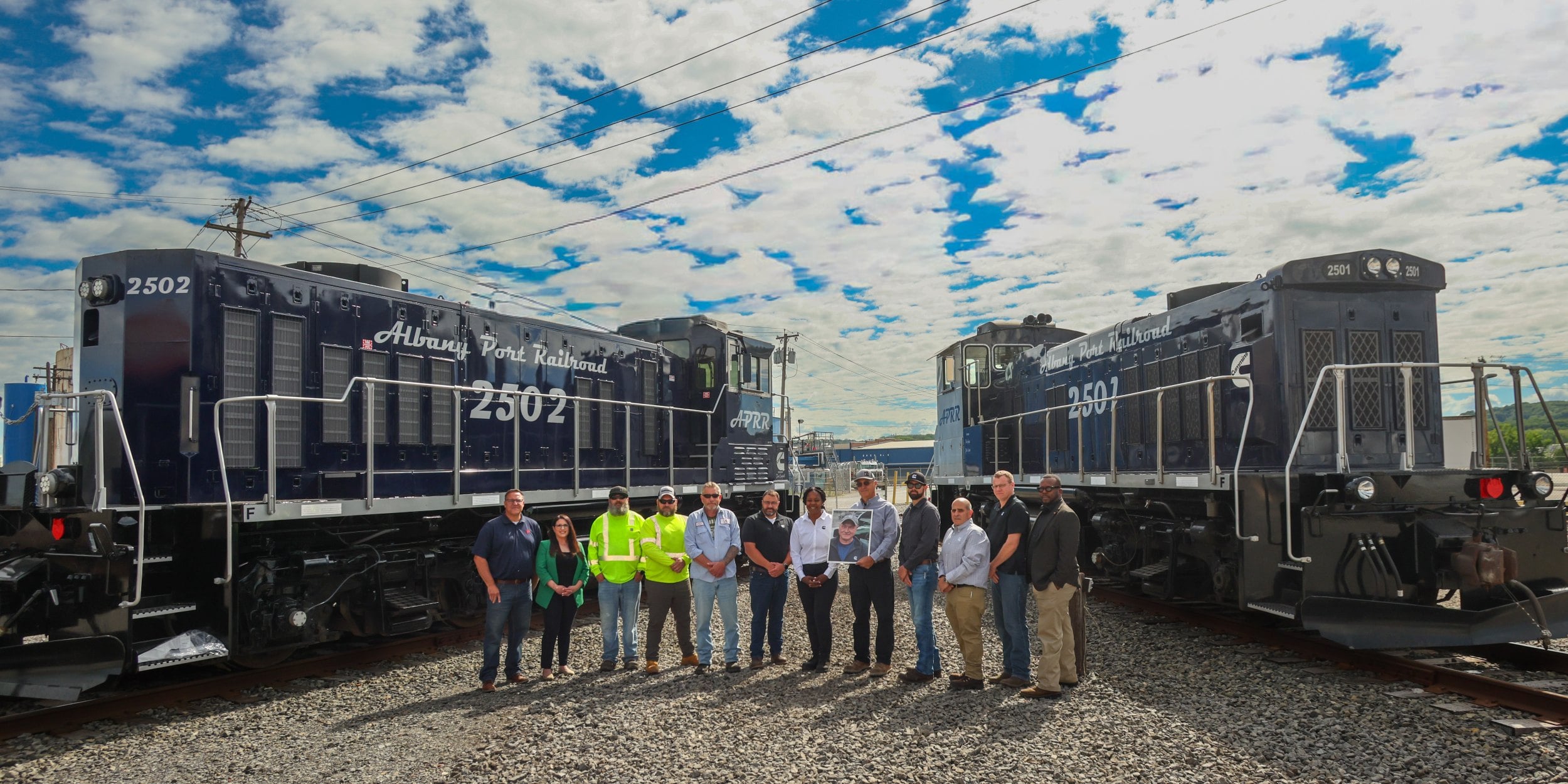 Albany Port Railroad team members pose between two locomotives at a rail yard as part of a locomotive modernization project