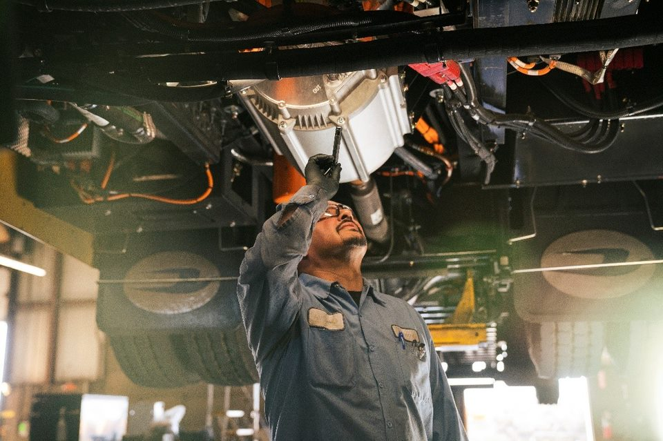 A technician working on the undercarriage of a Blue Bird electric school bus