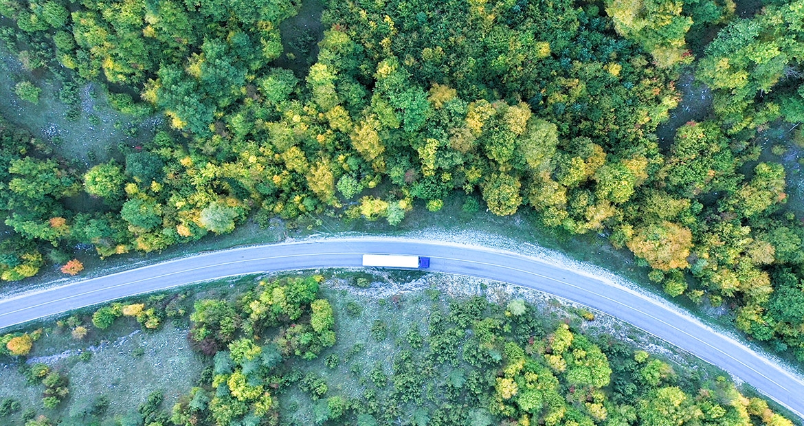 Un semi camion ce merge pe un drum șerpuit prin pădure